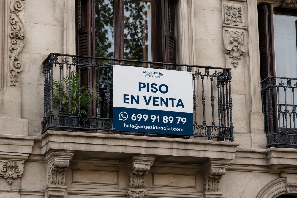 Balcony with ornate railing and a sign reading ‘Piso en venta’ with contact details below in blue and white.