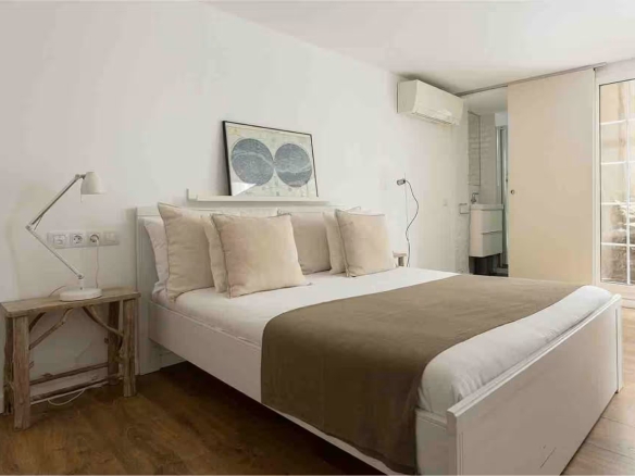 Hotel bedroom with a white bed, beige pillows, and a bedside lamp on a wooden table.