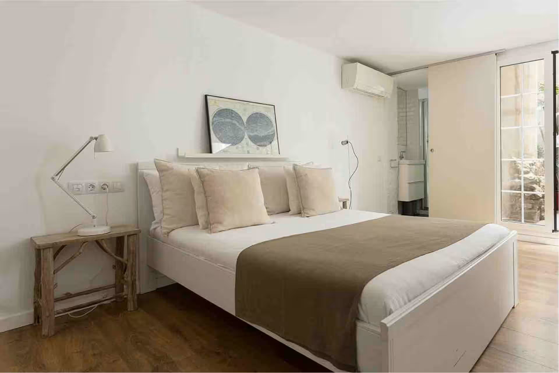 Hotel bedroom with a white bed, beige pillows, and a bedside lamp on a wooden table.