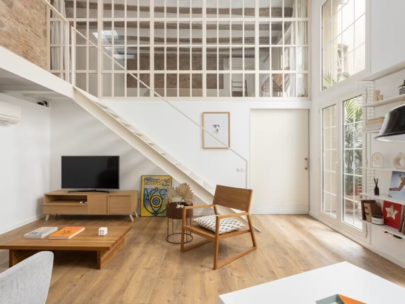 Bright open-plan living room with a loft, white staircase, and large windows letting in natural light.