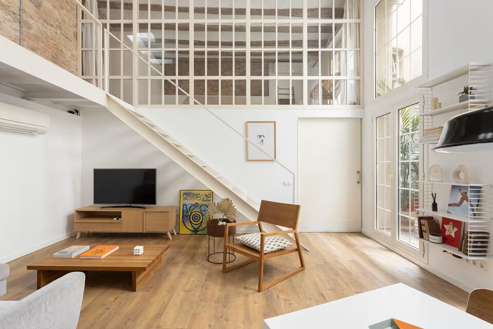 Bright open-plan living room with a loft, white staircase, and large windows letting in natural light.