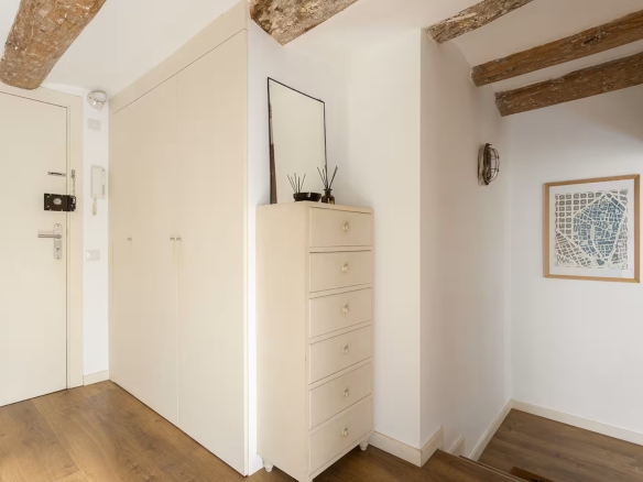 Bright entry hallway with exposed wooden ceiling beams, white walls, and a tall white dresser with a mirror on top.