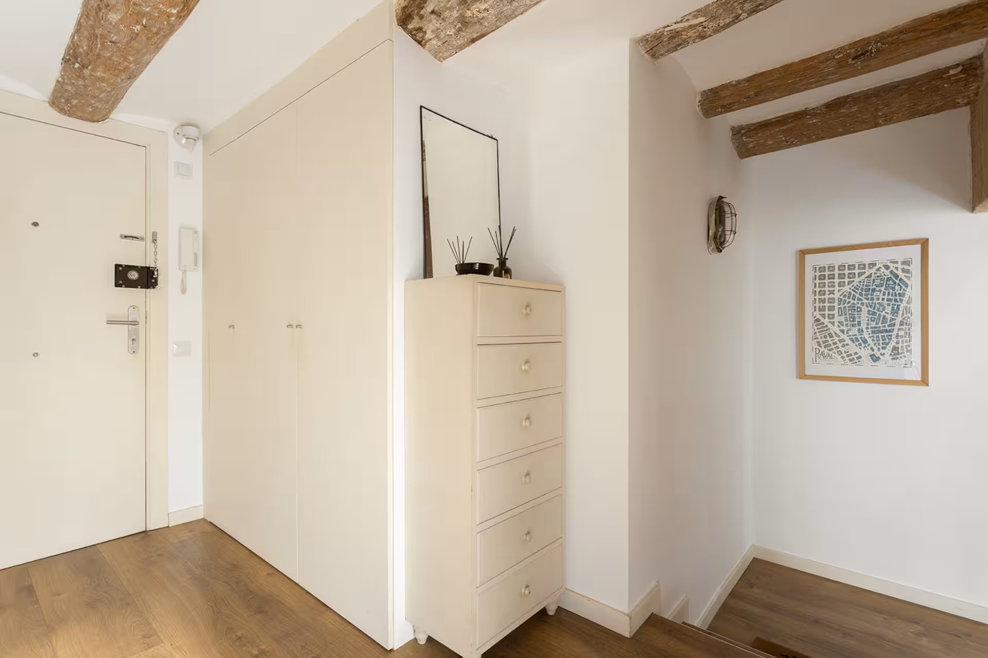 Bright entry hallway with exposed wooden ceiling beams, white walls, and a tall white dresser with a mirror on top.