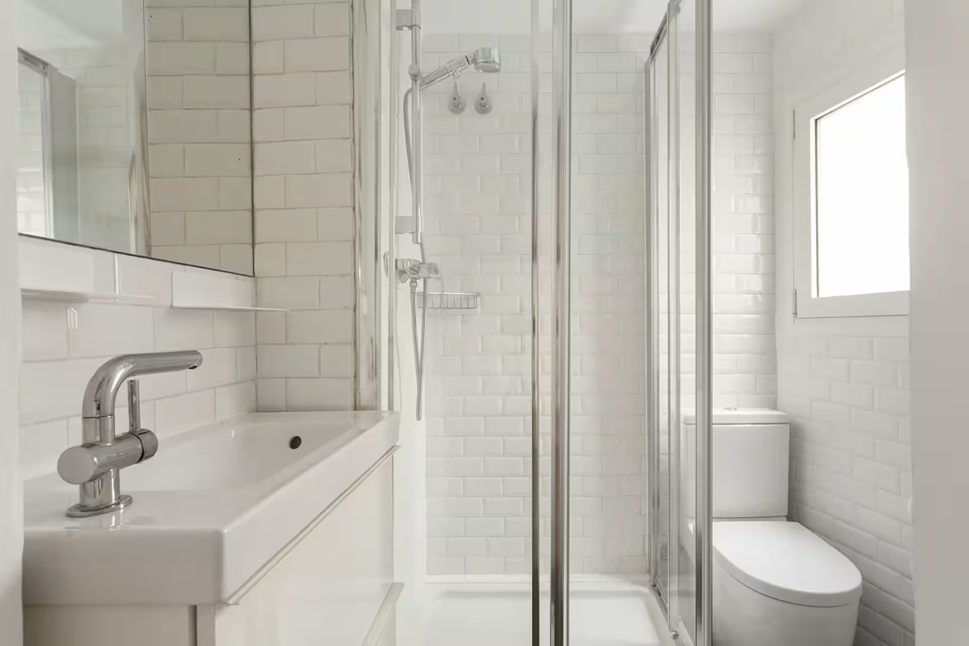 Bright white bathroom with a glass-enclosed shower, white subway tiles, and a white vanity.