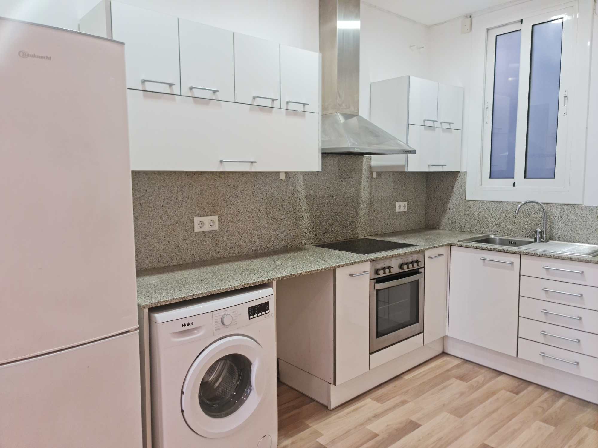 Modern white kitchen with gray-speckled granite counters, stainless steel range hood, oven, and washing machine.