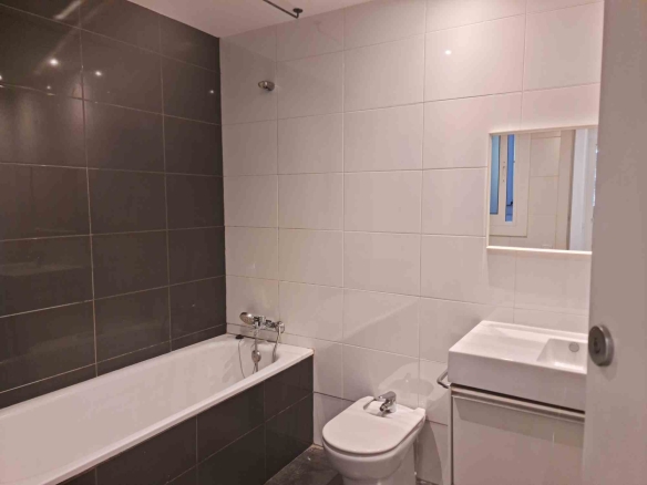 Modern bathroom with white wall tiles and a dark tile bathtub surround, featuring a bathtub, a toilet and bidet, and a wall mirror above a sink.