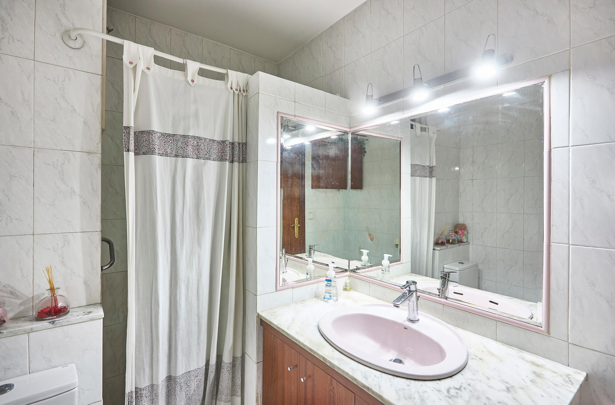 A modern bathroom with a pink-framed mirror above a marble countertop double sink and wooden vanity drawers.