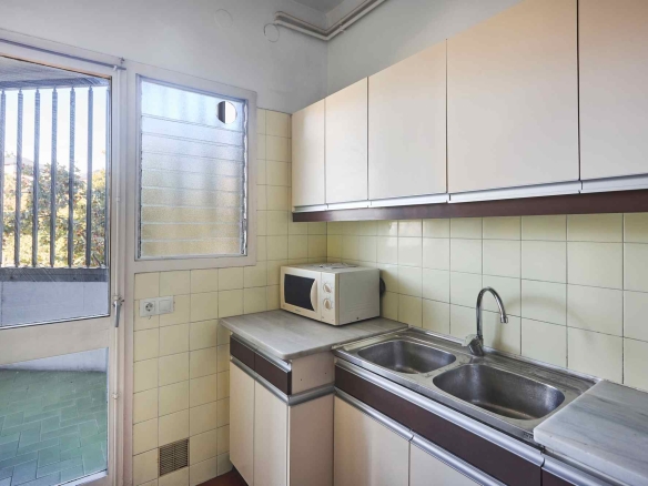 Small kitchen with cream cabinets, beige tiled backsplash, a double sink, and a microwave on the counter as part of the workspace outside a door window.