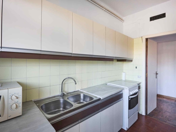 Kitchen with row of white wall cabinets above a pale tiled backsplash, stainless double sink, and white appliances along a marble countertop, doorway to adjacent room visible.