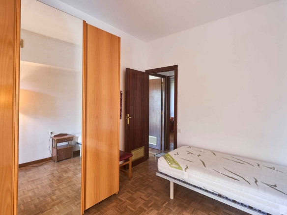 Bedroom with tall wooden wardrobes and a mirrored door, a bed at the edge, and an open doorway to another room.