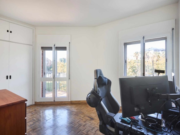 Bright home office with a desk, dual monitors, and an ergonomic chair by large windows; white cabinets along the left wall.