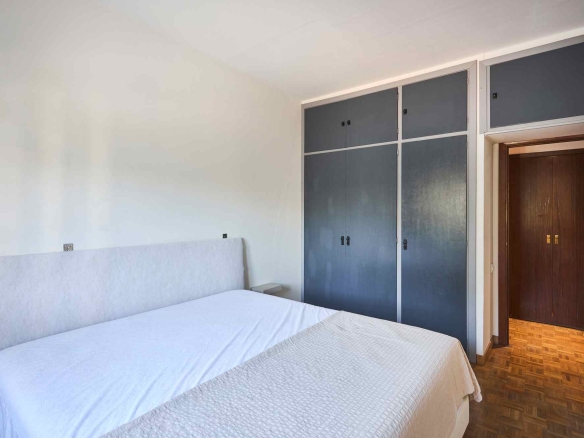 Two single beds with white quilts in a bright bedroom, opposite a wall of blue storage cabinets and a wooden doorway on the right.
