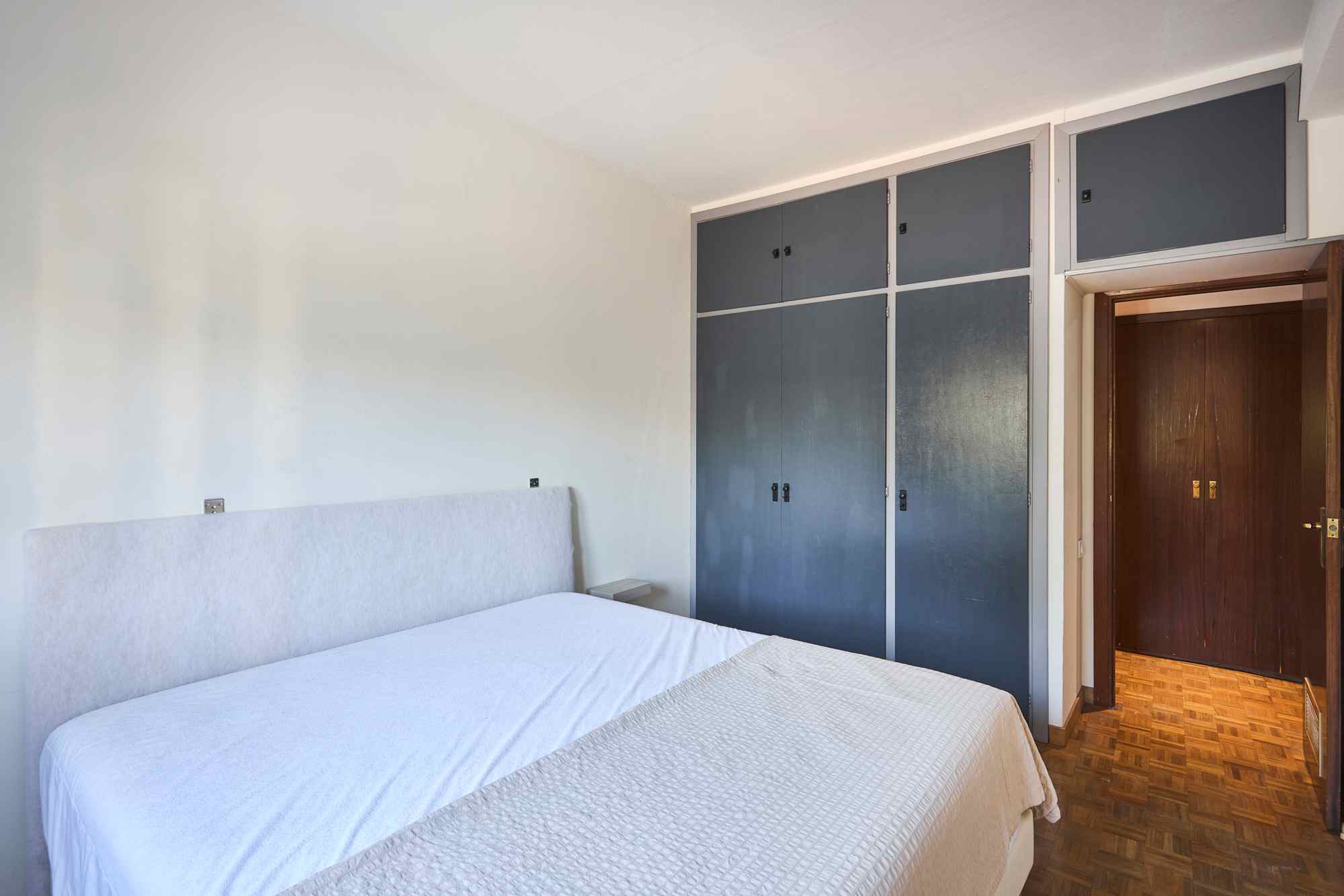 Two single beds with white quilts in a bright bedroom, opposite a wall of blue storage cabinets and a wooden doorway on the right.