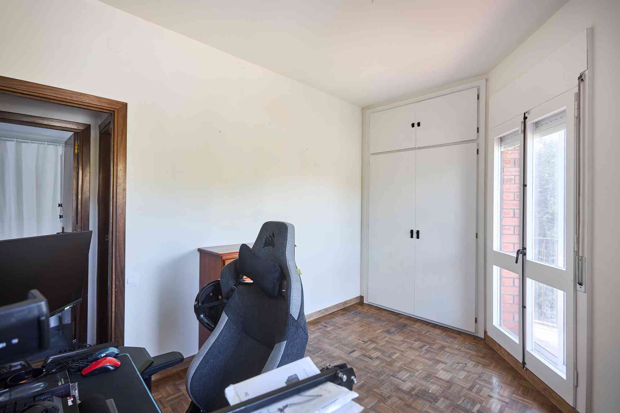 Home office corner with a desk, monitor, and ergonomic chair beside white built-in cabinets by a windowed door.",