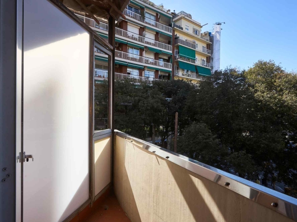 Balconies of an urban apartment building with green awnings seen from a small balcony and trees below, blue sky above.