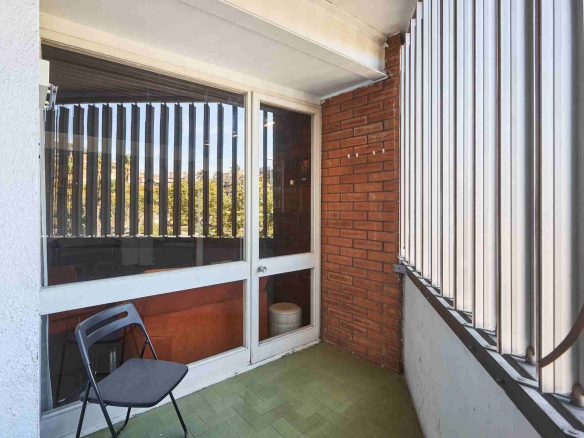 Balcony area with sliding glass doors, brick wall, and a black folding chair on a green tiled floor.